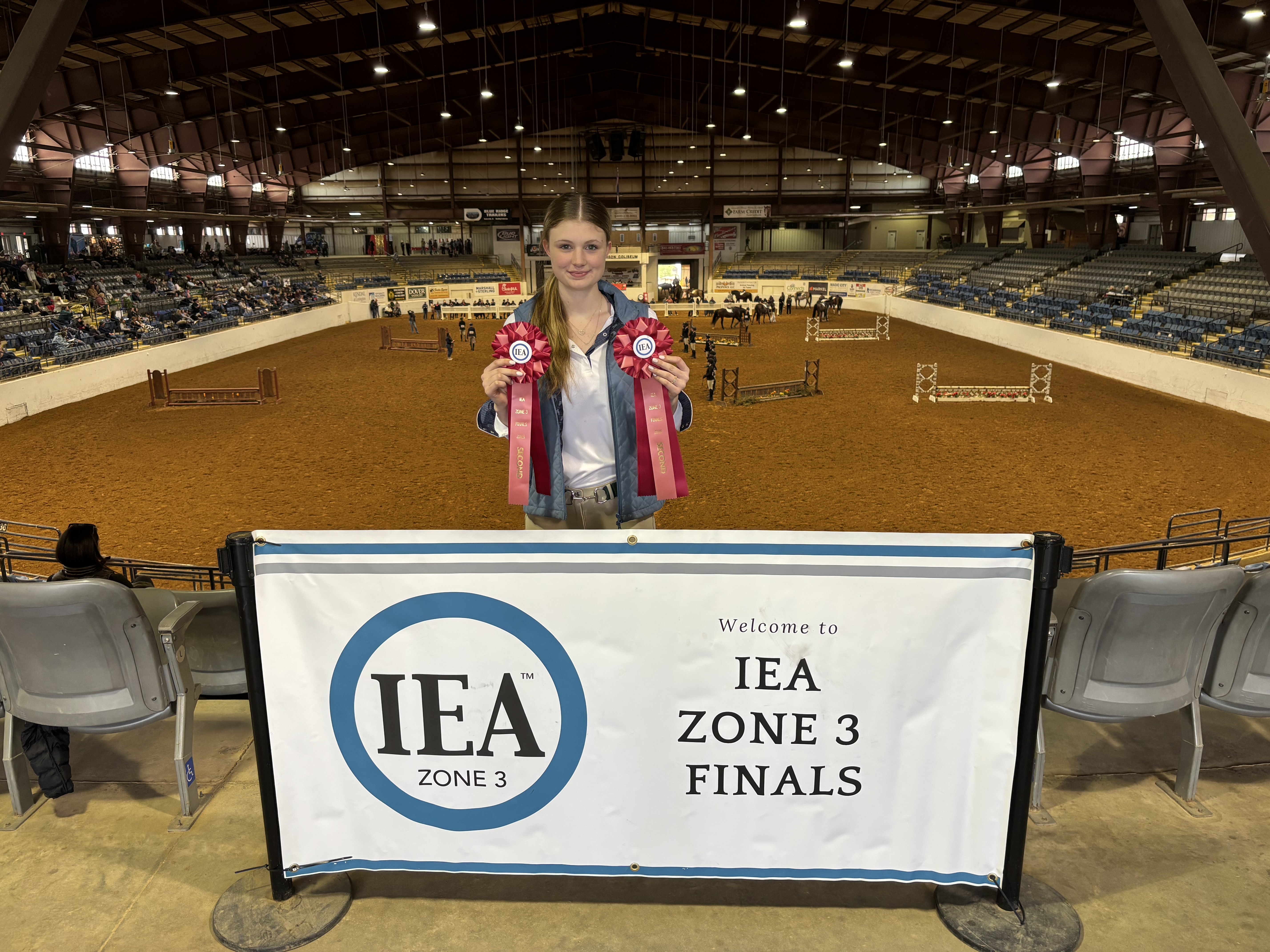 Lily holding both ribbons with the full IEA Zone 3 Finals ring behind her